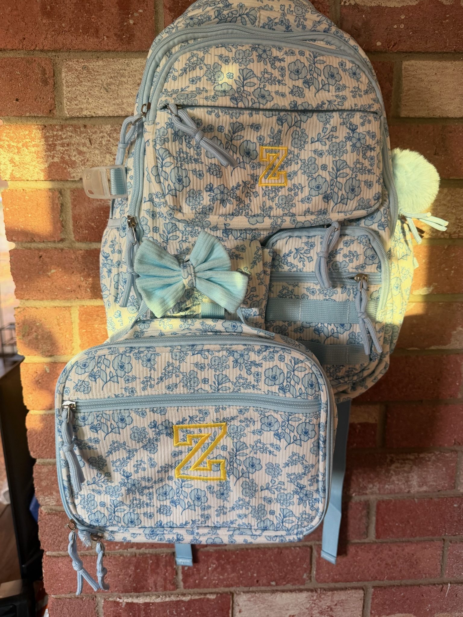 A floral corduroy backpack and its matching lunch box, each embroidered with a gold letter Z