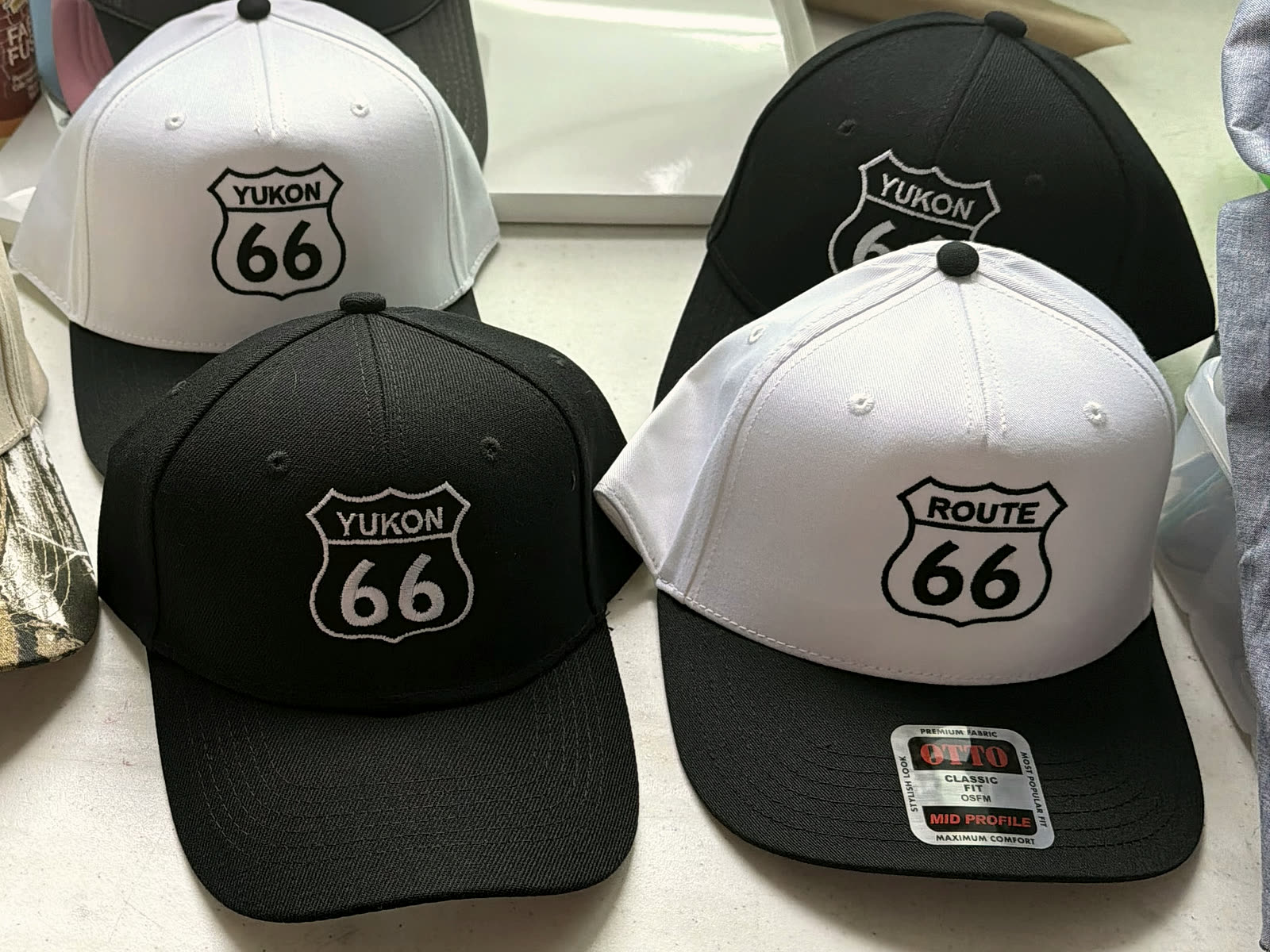 Four cream and black caps embroidered with YUKON 66 and ROUTE 66 shields, lined up on the workshop counter