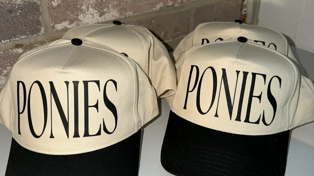 Matching cream caps with PONIES across the front, lined up on the counter against the brick