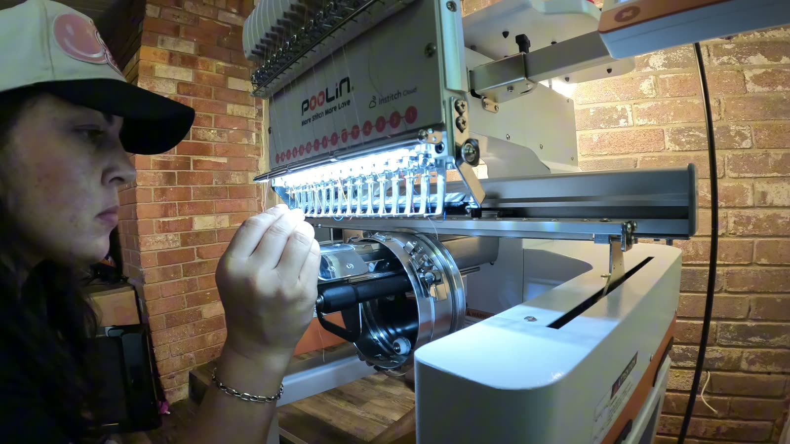 The maker at the needle bank of the embroidery machine, threading a color by hand