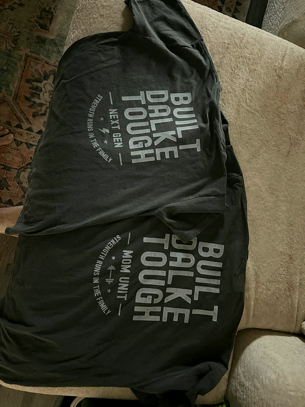 Black tees printed with stacked block lettering, folded over the arm of a chair after a run.