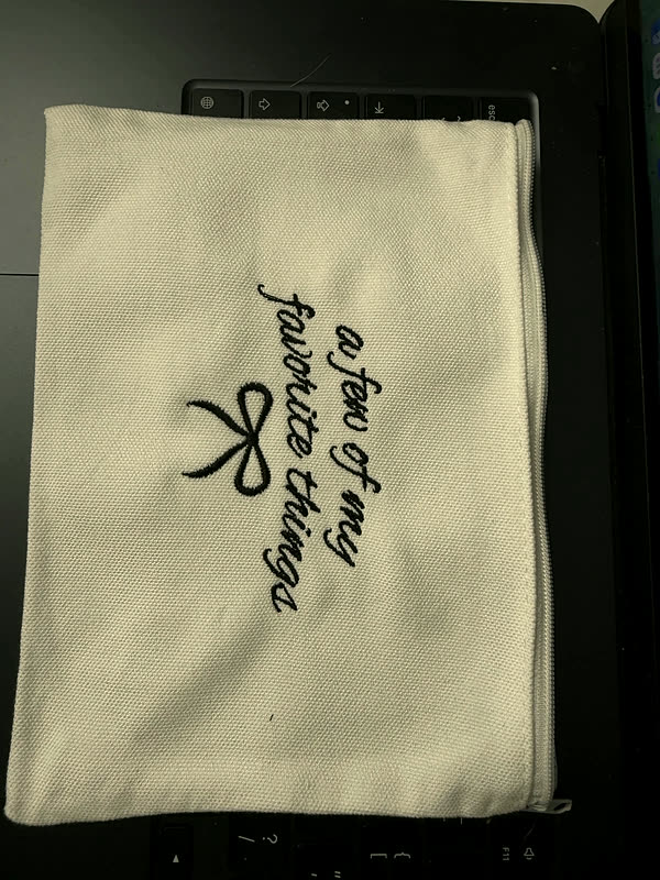 A cream canvas tote with a line of script and a small bow stitched down one side.