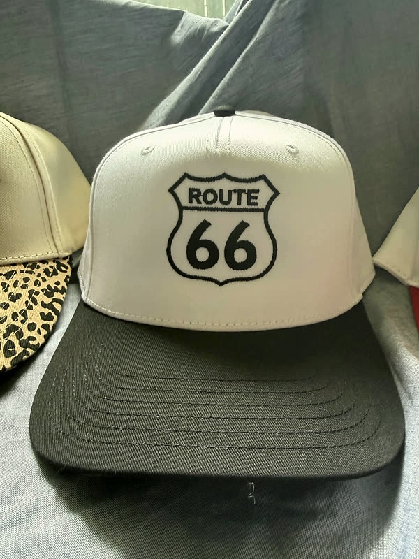 A cream cap with a black brim and a single stitched highway shield on the front panel.