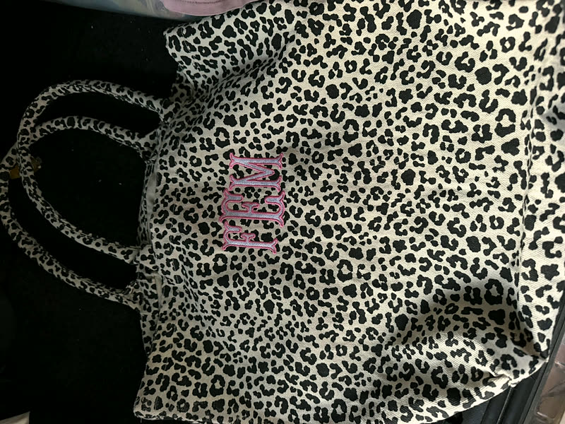 An animal-print tote with a short word stitched in pink on the side panel.