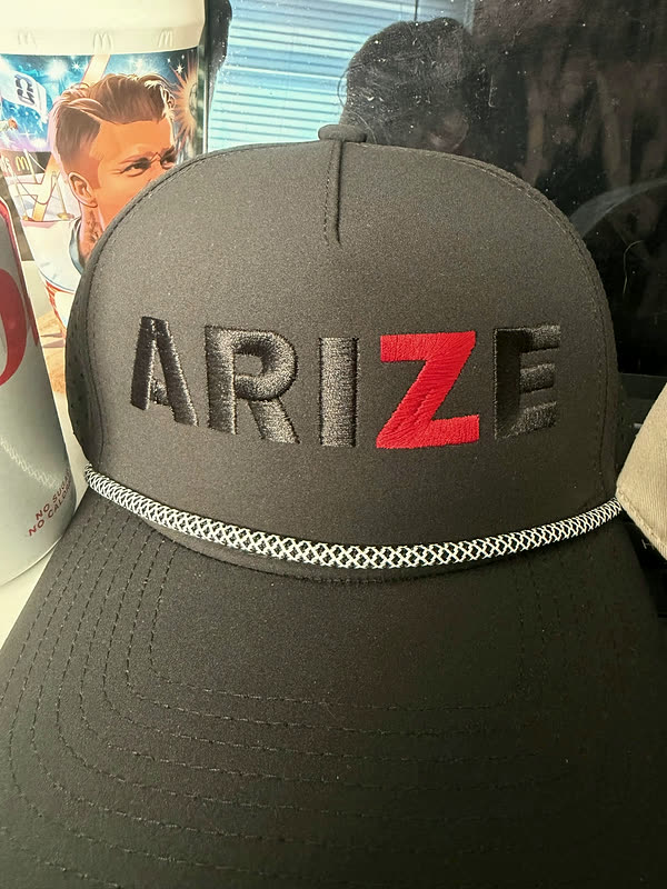 A brown rope cap with the same five-letter wordmark stitched in tonal thread, the last letter picked out in red.