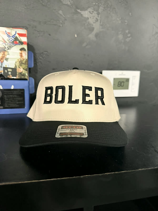 A cream and black cap with a single name stitched in tall block letters across the front.