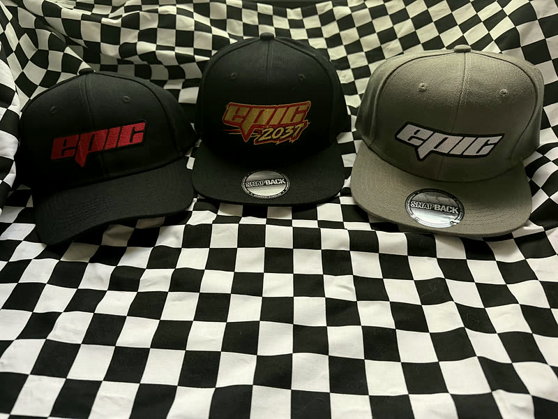 Three caps with the same stitched wordmark, two black and one grey, arranged on a black and white checkered cloth.