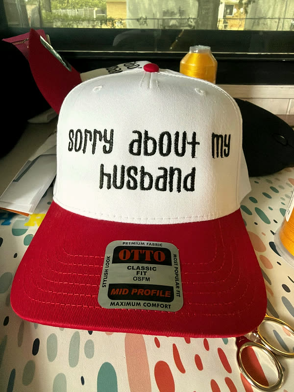 A white and red trucker cap with a two-line phrase stitched across the front panel in black.