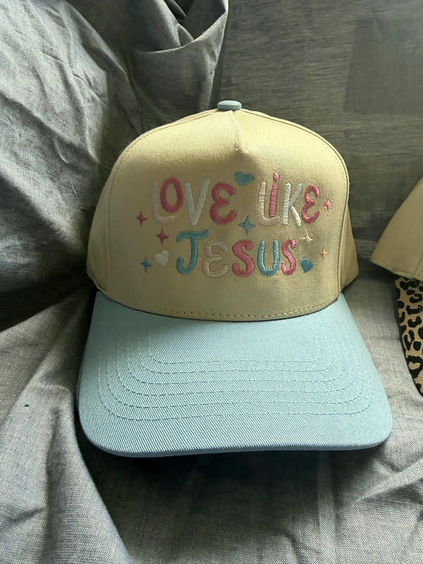 A pale yellow cap with a light blue brim and a phrase stitched across the crown in pastel thread with small hearts.