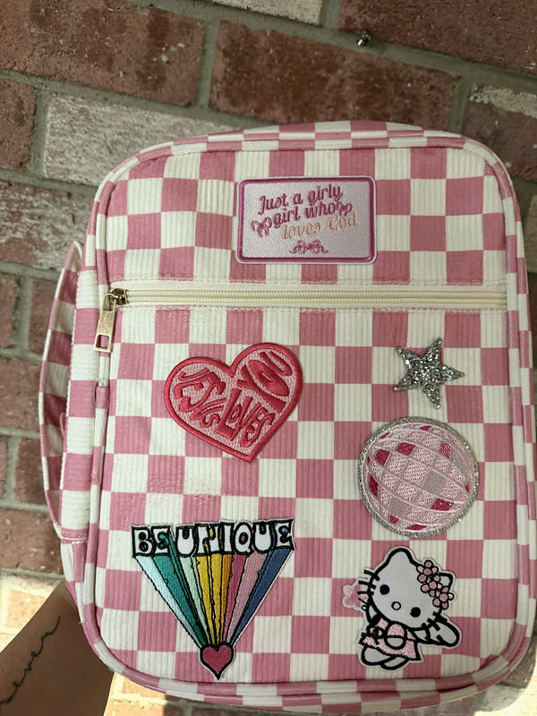 A pink and white checkerboard backpack with a heart, a rainbow and a full-color character patch.