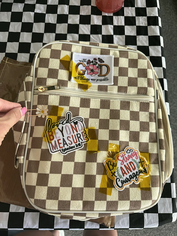 A brown and cream checkerboard zip case with a daisy, a word panel and two smaller patches.