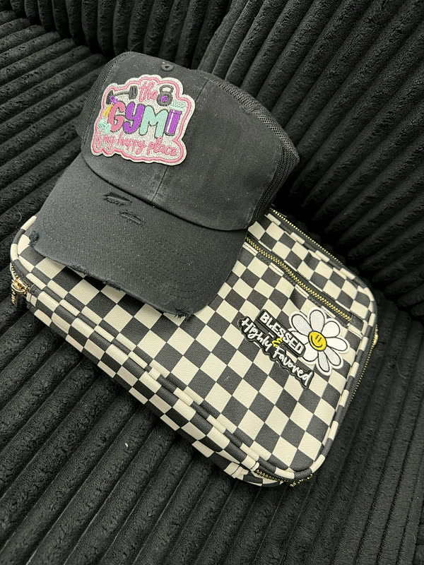 A charcoal cap with a word patch resting on a black and white checkerboard case with a daisy.