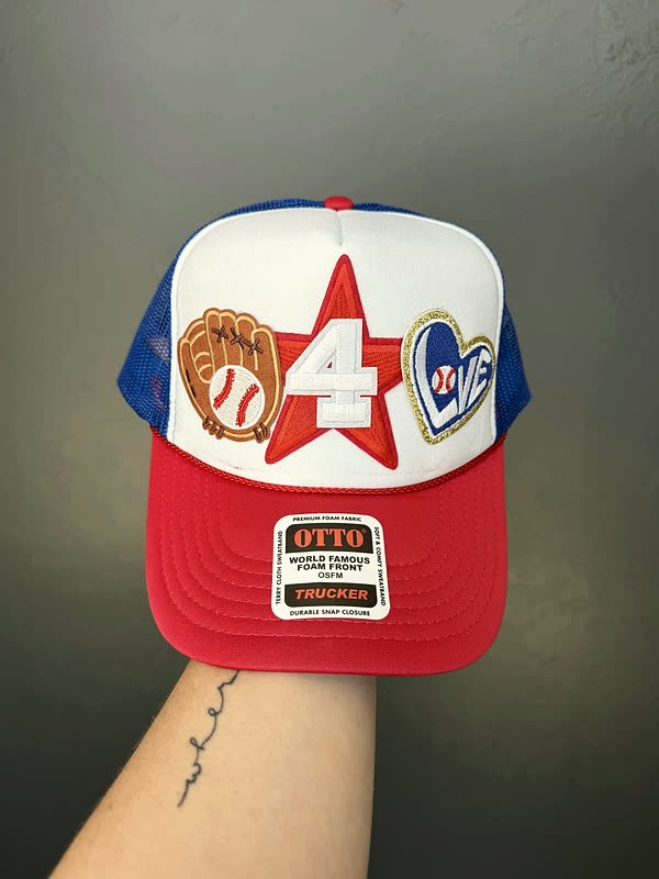 A red, white and blue trucker cap with a large star, a glove, a number and a heart patched across the front.