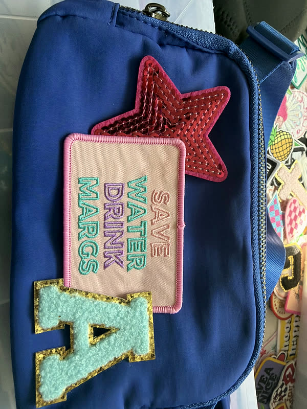 A blue belt bag with a chenille star, a chenille letter and a rectangular word patch.