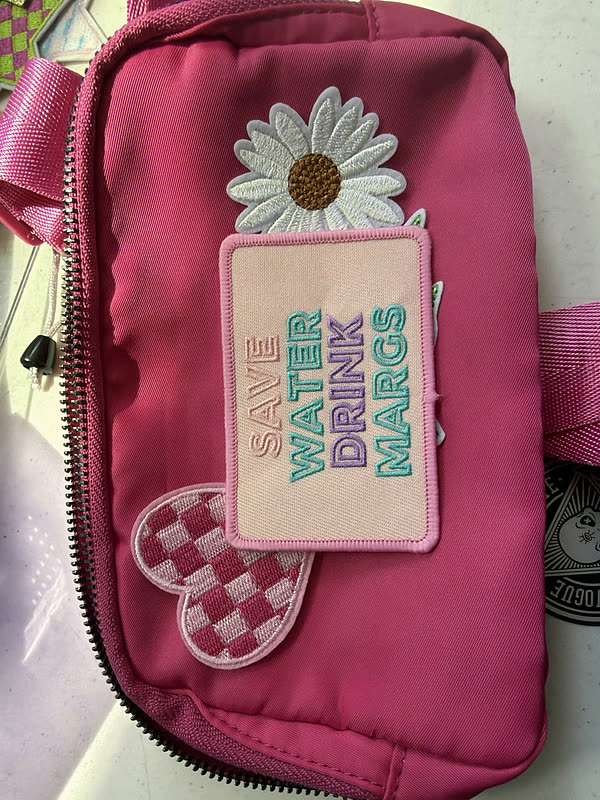 A pink belt bag with a large daisy patch and a rectangular word patch beside it.
