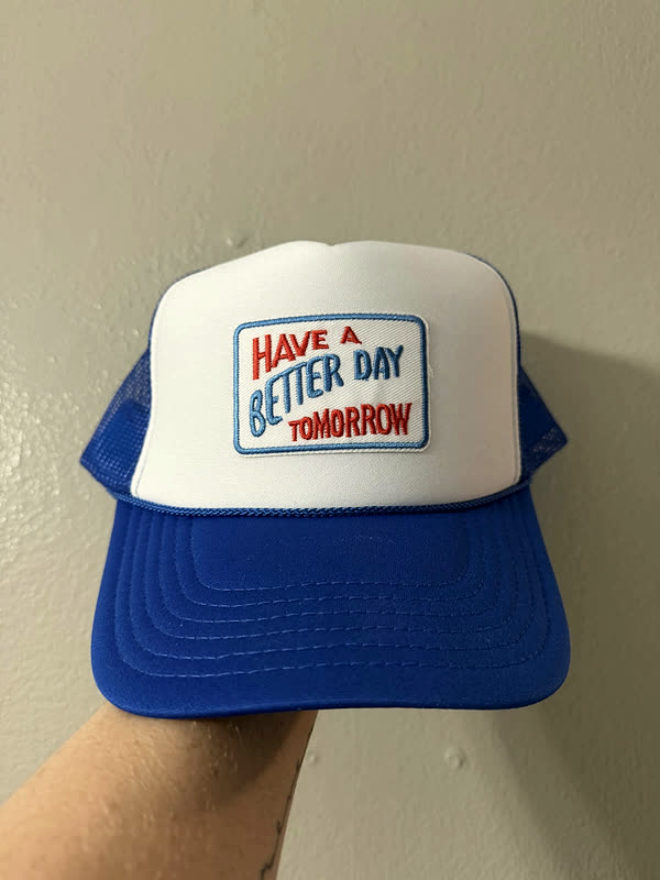 A white and blue trucker cap with a rectangular word patch across the front panel.