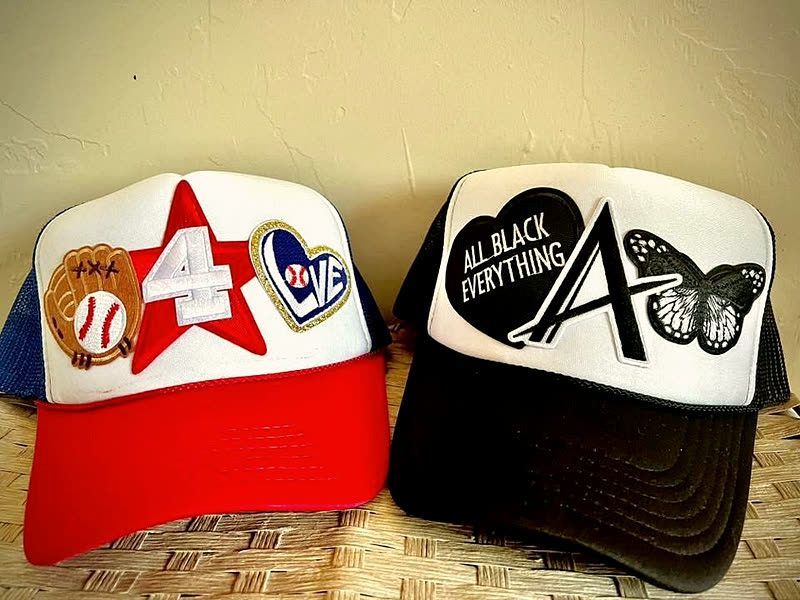 A red trucker with a star patch and a black trucker with a butterfly patch, lying side by side on woven matting.
