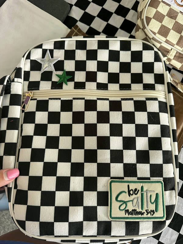 A black and white checkerboard bag with a star patch at the top corner and a small script patch near the base.