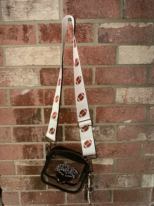 A clear stadium bag hanging on a brick wall by a printed strap, with a sequin patch on the front panel.