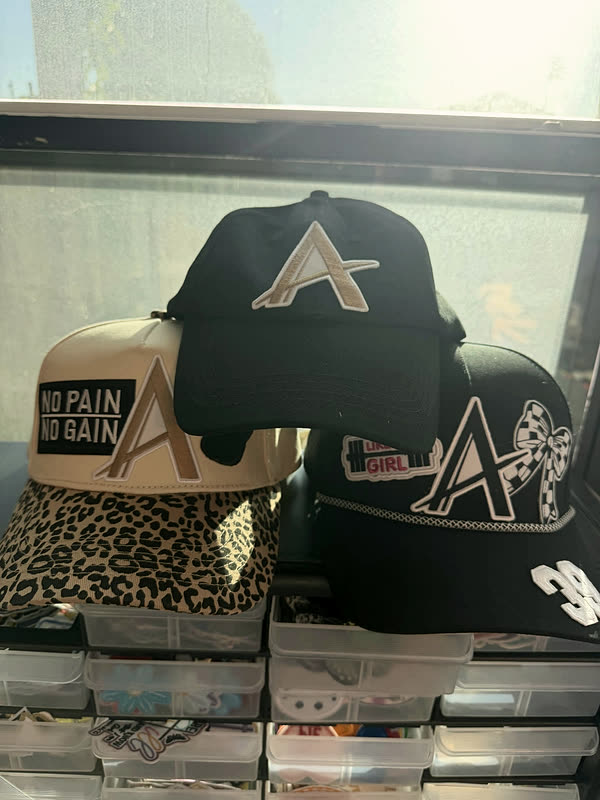 Several patched caps in black, camo, leopard and cream lined up on a shelf above storage drawers.