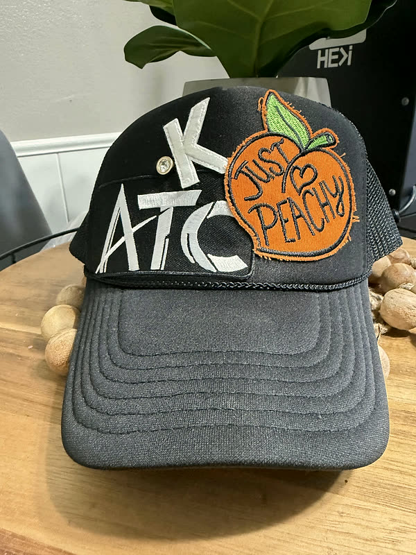 A charcoal cap with a three-letter patch and a round fruit patch set beside it.