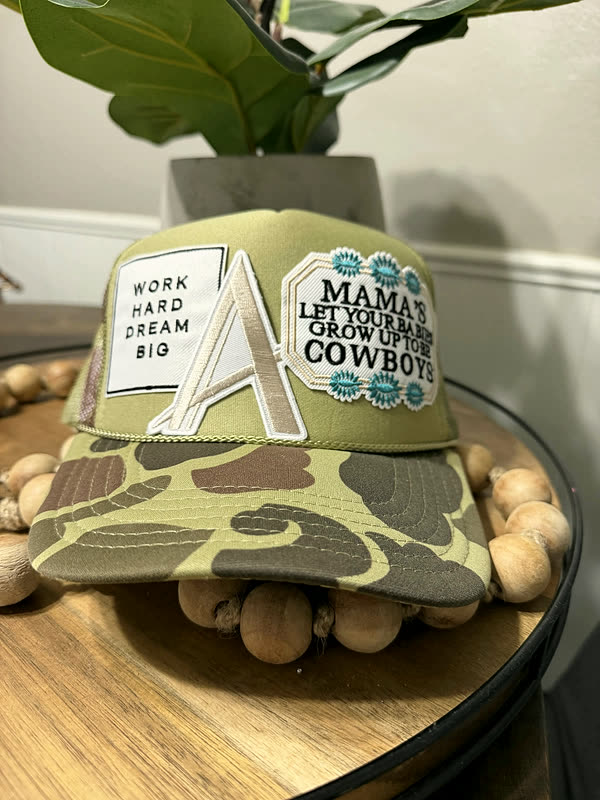 An olive camo cap with two rectangular word patches and a chenille letter across the front.