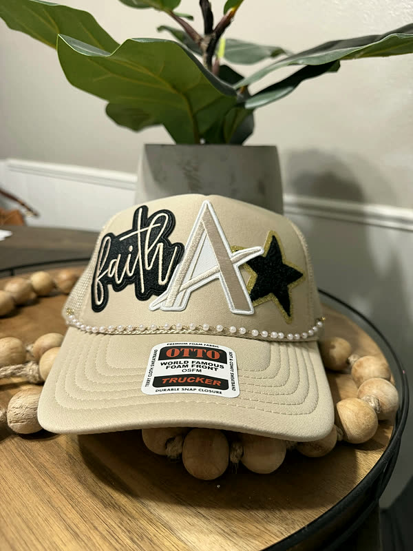 A cream cap with script lettering, a chenille letter and a black star, standing on a wood tray.