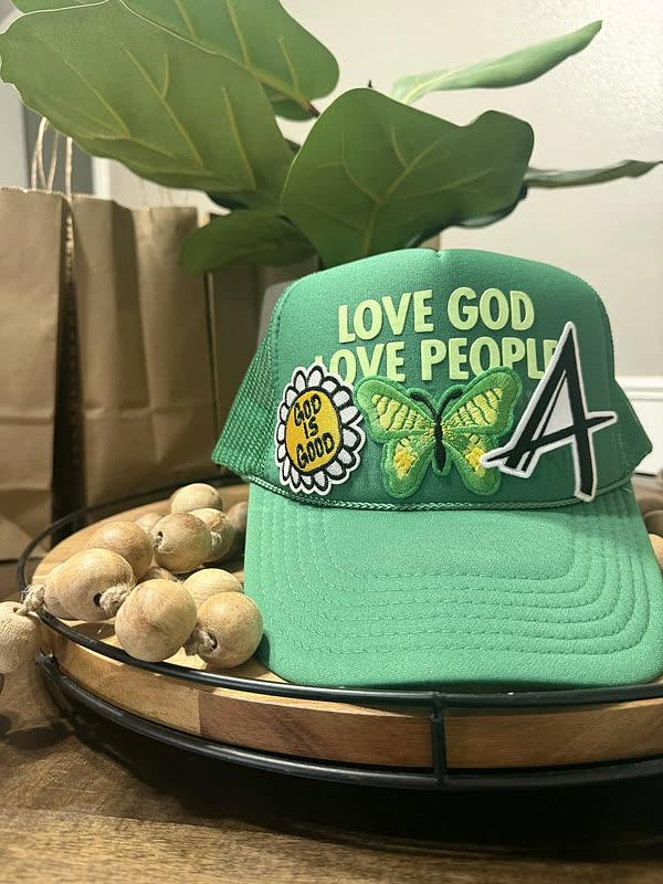 A green cap with a word patch, a butterfly and a chenille letter across the front panel.