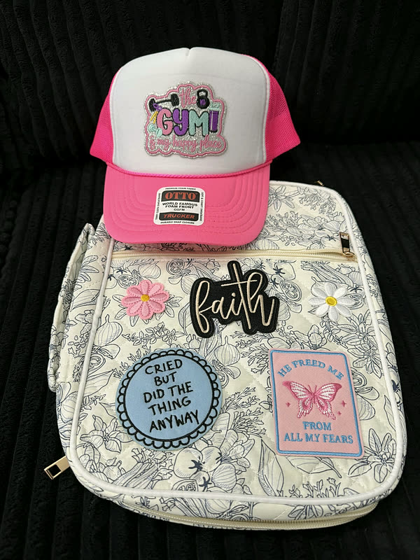 A pink trucker cap with a chenille patch lying on a pale floral book cover that carries three word patches.