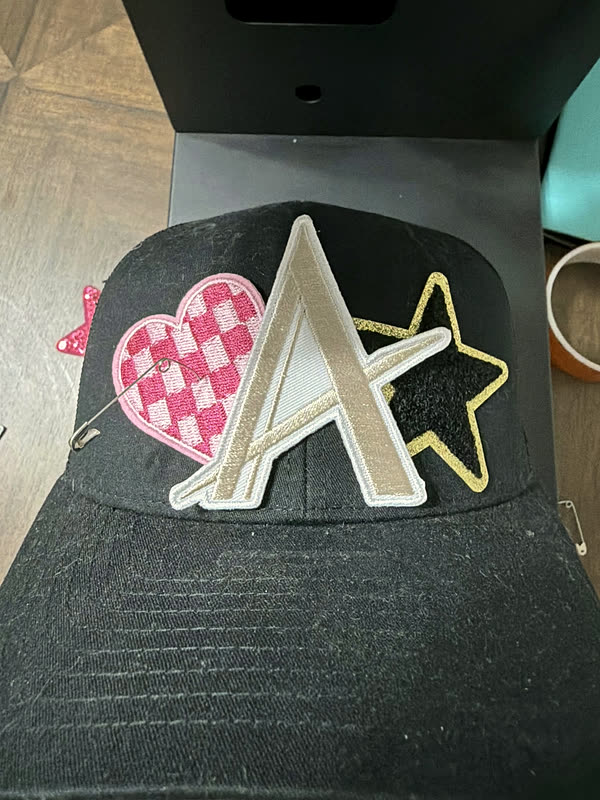 A charcoal cap lying open in a heat press, script lettering and a star patch laid in place under the platen.