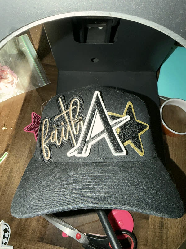 The same charcoal cap in the heat press from a second angle, the script lettering and star positioned on the crown.