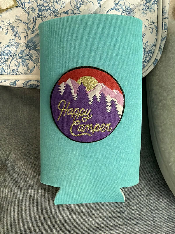 A teal can koozie with a round mountain-scene patch.