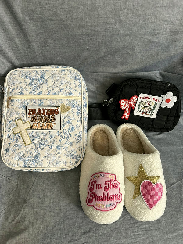 A floral book cover, a small zip case and a pair of cream sherpa slippers laid out together, each carrying patches.