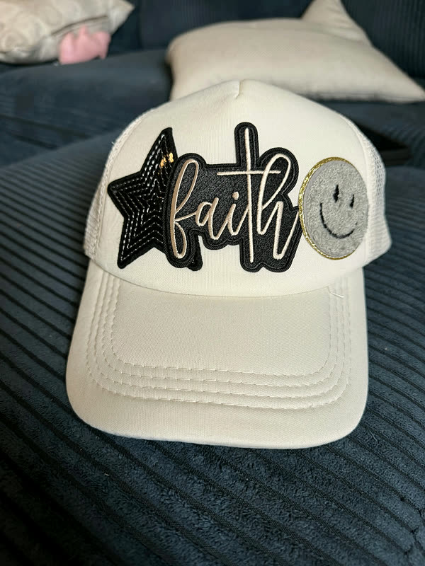 A cream cap with a black star, script lettering and a small smiley patch.