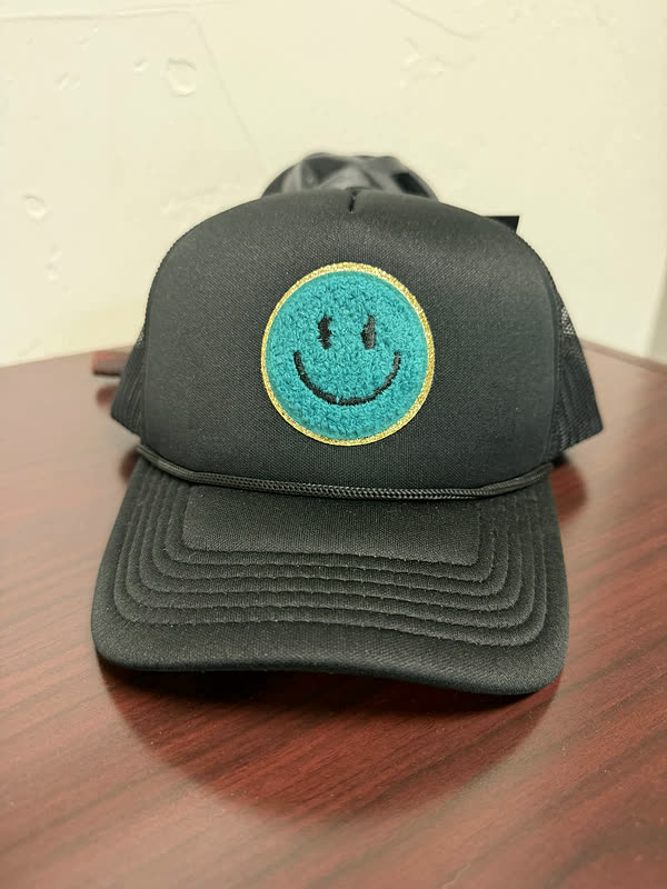 A charcoal cap with a single round teal chenille smiley patch on the front panel.