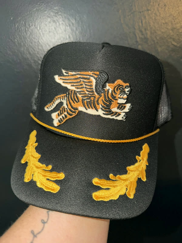 A black rope cap with a leaping tiger patch on the crown and gold laurel embroidery worked across the brim.