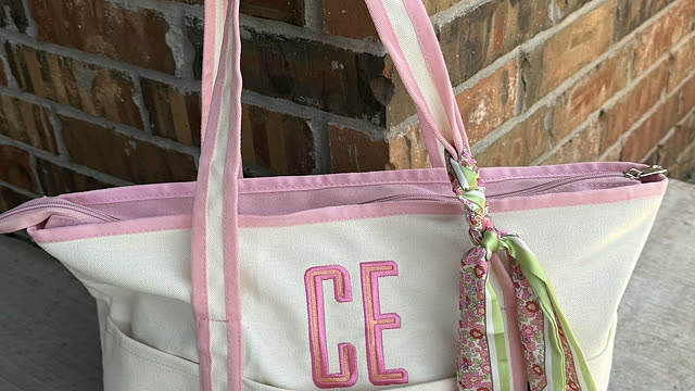 A cream and pink tote bag with a monogram stitched across the front pocket