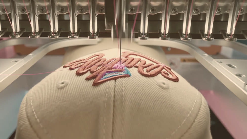 Placeholder image: a needle stitching red thread into a cap crown